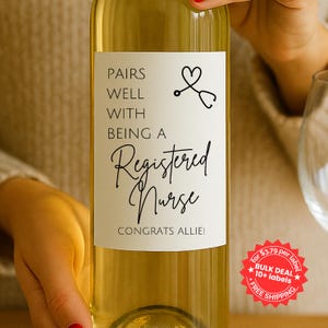 May include: A white wine bottle with a custom label. The label reads "PAIRS WELL WITH BEING A Registered Nurse CONGRATS ALLIE!" in black script. A stethoscope and heart graphic is also on the label.