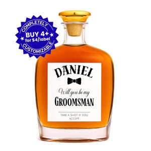 May include: A clear glass bottle filled with amber liquid, featuring a gold cap and a cork stopper. The label reads "DANIEL" above a bow tie graphic, with "Will you be my GROOMSMAN" below. The text "TAKE A SHOT IF YOU ACCEPT" is at the bottom.