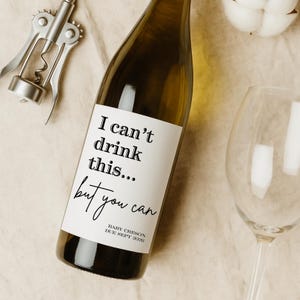 May include: A wine bottle with a custom label that reads "I can't drink this... but you can." A silver corkscrew and a wine glass are next to the bottle. The label also includes "BABY CRESON DUE SEPT 2026."
