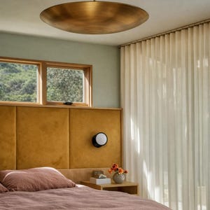 K&ouml;nnte beinhalten: Schlafzimmer mit einer gro&szlig;en, bronzefarbenen Deckenleuchte. Das Zimmer verf&uuml;gt &uuml;ber ein senffarbenes Kopfteil, ein Bett mit einer staubrosa Bettdecke und einen kleinen Nachttisch mit einer Lampe. Transparente wei&szlig;e Vorh&auml;nge h&auml;ngen im Hintergrund.