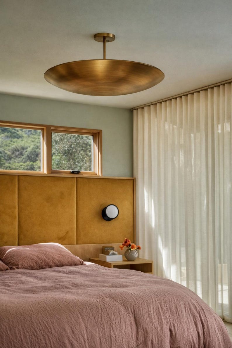 K&ouml;nnte beinhalten: Schlafzimmer mit einer gro&szlig;en, bronzefarbenen Deckenleuchte. Das Zimmer verf&uuml;gt &uuml;ber ein senffarbenes Kopfteil, ein Bett mit einer staubrosa Bettdecke und einen kleinen Nachttisch mit einer Lampe. Transparente wei&szlig;e Vorh&auml;nge h&auml;ngen im Hintergrund.