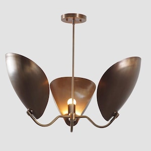 Op de afbeelding: Een bronzen hanglamp met drie lampen. De lamp heeft een centrale kegelvormige kap en twee vleugelvormige kappen aan weerszijden. De lamp hangt aan een plafondplaat met een slanke stang. Gemaakt van metaal.