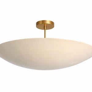 K&ouml;nnte beinhalten: Eine moderne Deckenleuchte mit einem cremefarbenen, ovalen Schirm. Die Leuchte wird von einer goldfarbenen, kreisf&ouml;rmigen Basis und einer schlanken Stange abgeh&auml;ngt. Das Design ist minimalistisch und elegant, passend f&uuml;r verschiedene Einrichtungsstile. Ca. 60 cm lang.