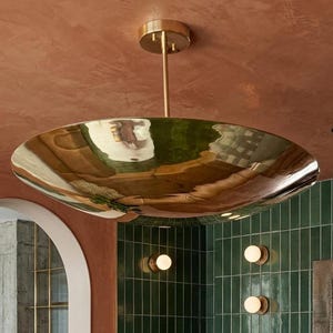 K&ouml;nnte beinhalten: Eine gro&szlig;e, goldfarbene, schalenf&ouml;rmige Deckenleuchte, die an einer bronzefarbenen Stange und Deckenhalterung aufgeh&auml;ngt ist. Das Licht reflektiert die Umgebung. Der Hintergrund zeigt eine gr&uuml;ne geflieste Wand und eine rotbraune Decke.