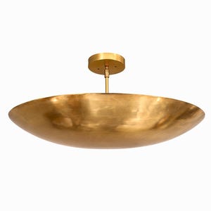 K&ouml;nnte beinhalten: Eine gro&szlig;e, goldfarbene Deckenleuchte mit einem flachen, schalenf&ouml;rmigen Schirm. Die Leuchte wird von einer runden, goldfarbenen Deckenhalterung durch eine schlanke Stange abgeh&auml;ngt. Der Schirm hat eine glatte, reflektierende Oberfl&auml;che.