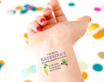 Könnte beinhalten: Ein temporäres Tattoo mit dem Text "I'm with Katerina's Bachelorette Party." Das Tattoo enthält auch einen Cocktail, eine Palme und eine violette und grüne Masken.
