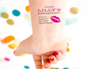 Può includere: Un tatuaggio temporaneo su un polso con la scritta "I'M WITH LILLY'S BACHELORETTE PARTY." Il tatuaggio include anche la scritta "IF I'M LOST, PLEASE BUY ME A DRINK THEN RETURN ME!" e una grafica di labbra rosa. Le unghie della persona sono dipinte di rosso.