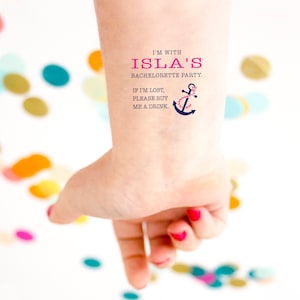Può includere: Tatuaggio temporaneo su un polso con la scritta "I'M WITH ISLA'S BACHELORETTE PARTY. IF I'M LOST, PLEASE BUY ME A DRINK." È presente anche un'ancora con una corda rosa. Lo sfondo è bianco con coriandoli colorati.
