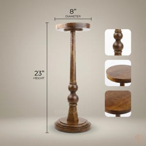 May include: A wooden plant stand with a round top and base. The stand is 23 inches tall and the top is 8 inches in diameter. The stand has a dark brown finish and a decorative, turned design. The text "treewood" is visible on the stand.