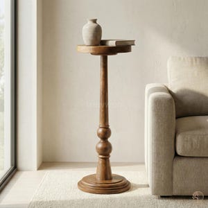 May include: A tall, wooden side table with a round top and base. The table has a slender, turned column with decorative spheres. A small, beige vase and a book rest on the tabletop. The table is approximately 30 inches tall.