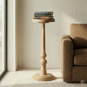 May include: A tall, light-colored wooden side table with a round top and base. The table has a slender, turned column with two decorative spheres. Three books are stacked on the top. The table is next to a brown sofa.