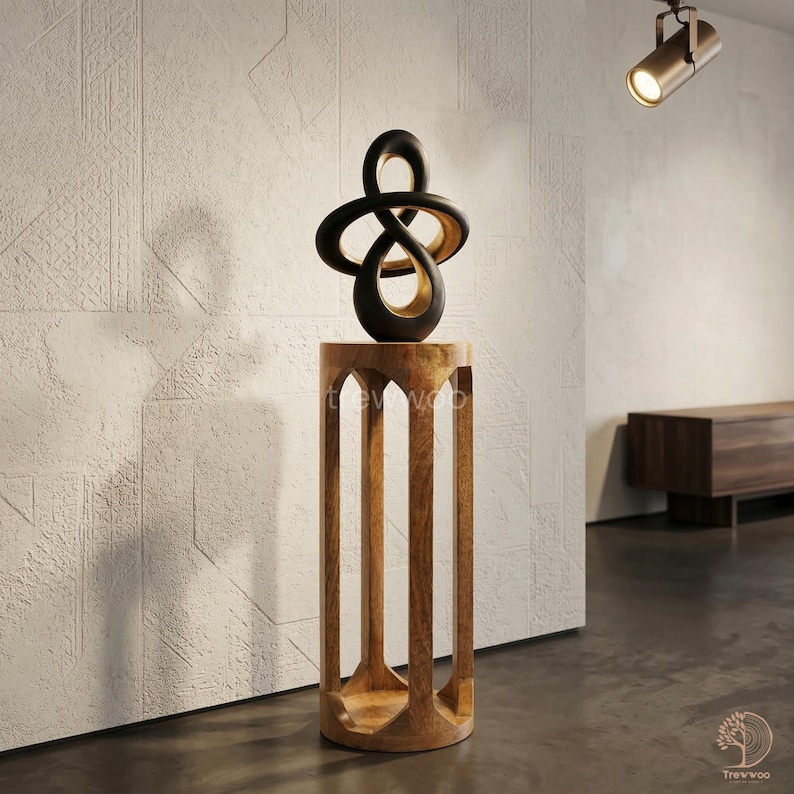 Op de afbeelding: Een moderne sculptuur met een zwart en goud ontwerp staat op een houten sokkel. De sokkel heeft een cilindrische vorm met boogvormige uitsparingen. De abstracte sculptuur voegt een eigentijdse touch toe aan de kamerdecoratie. De sokkel is ongeveer 76 cm hoog.