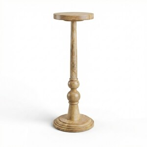 May include: A light brown wooden pedestal table with a round top, a long, slender stem, and a decorative base. The table stands approximately 30 inches tall.