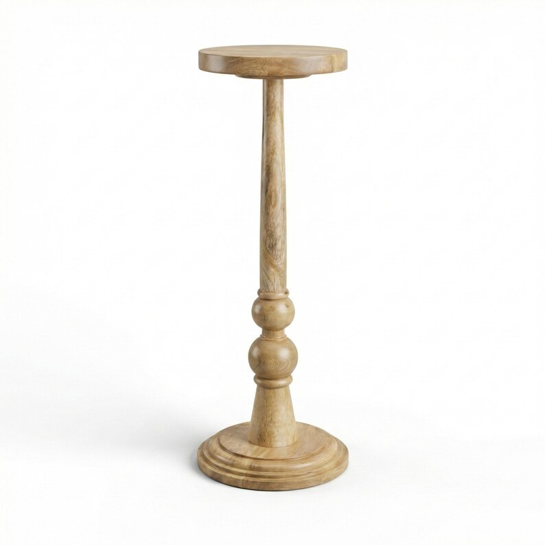 May include: A light brown wooden pedestal table with a round top, a long, slender stem, and a decorative base. The table stands approximately 30 inches tall.