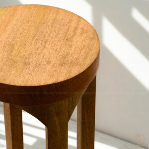 Op de afbeelding: Houten kruk met een ronde zitting en drie poten. De kruk is gemaakt van lichtbruin hout en heeft een natuurlijk houtnerfpatroon. Het ontwerp is eenvoudig en modern, geschikt voor diverse interieurstijlen. Hoogte ongeveer 45 cm.