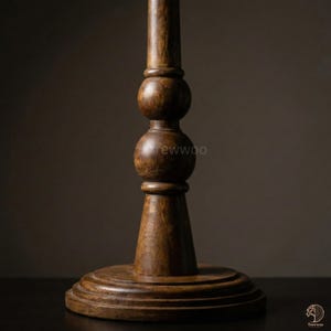 May include: A close-up of a wooden table leg with a dark brown finish. The leg features a turned design with a round base and a series of decorative spheres. The wood grain is visible, adding texture to the piece. The overall aesthetic is rustic and elegant.