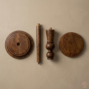 May include: Four wooden furniture components, including two circular pieces, a long, cylindrical leg, and a decorative, turned leg. The wood has a warm, brown stain. The pieces are arranged against a neutral background, suggesting a DIY furniture project.