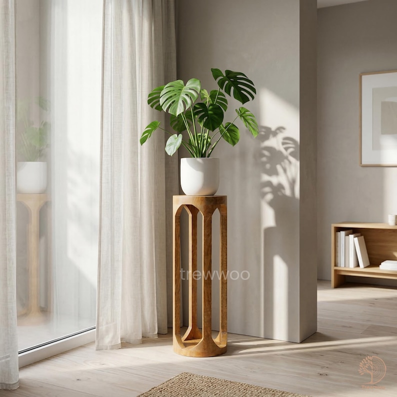Op de afbeelding: Een houten plantenstandaard met een witte pot met een groene Monstera-plant. De standaard heeft een open ontwerp met verticale steunen. De kamer heeft een neutraal kleurenpalet en natuurlijk licht. De standaard is ongeveer 100 cm hoog.