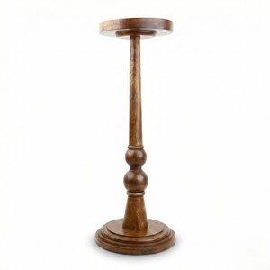 May include: A wooden plant stand with a round top and base, connected by a slender, turned column. The column features two decorative spherical elements. The stand is approximately 30 inches tall.