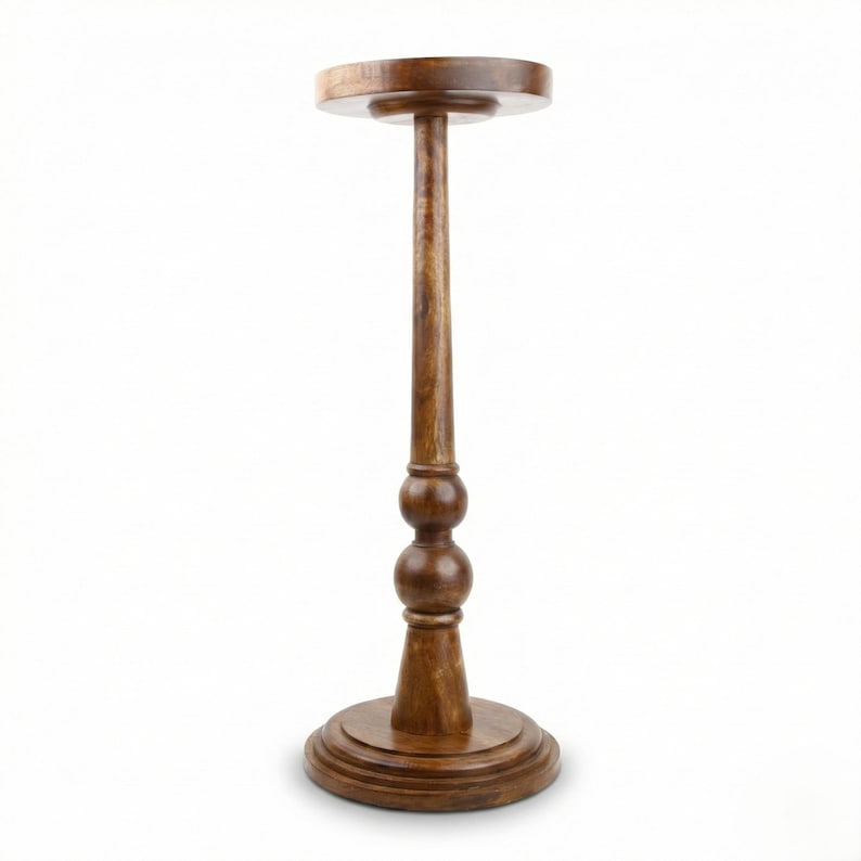 May include: A wooden plant stand with a round top and base, connected by a slender, turned column. The column features two decorative spherical elements. The stand is approximately 30 inches tall.