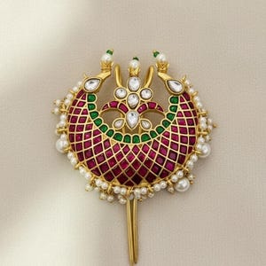 Op de afbeelding: Goudkleurig haaraccessoire met een halvemaanvormig ontwerp. Het stuk heeft een centraal gedeelte van rode en groene edelstenen, omringd door parels. De bovenkant heeft drie decoratieve elementen met witte edelstenen en parels, en een lange, gouden pin.