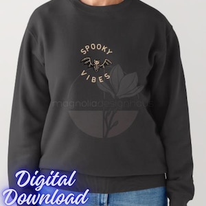 Pu&ograve; includere: Felpa grigio scuro con le parole "Spooky Vibes" e una grafica a pipistrello. Il design include un elemento floreale e il testo "magnoliadesignhaus". Sono visibili anche le parole "Digital Download".