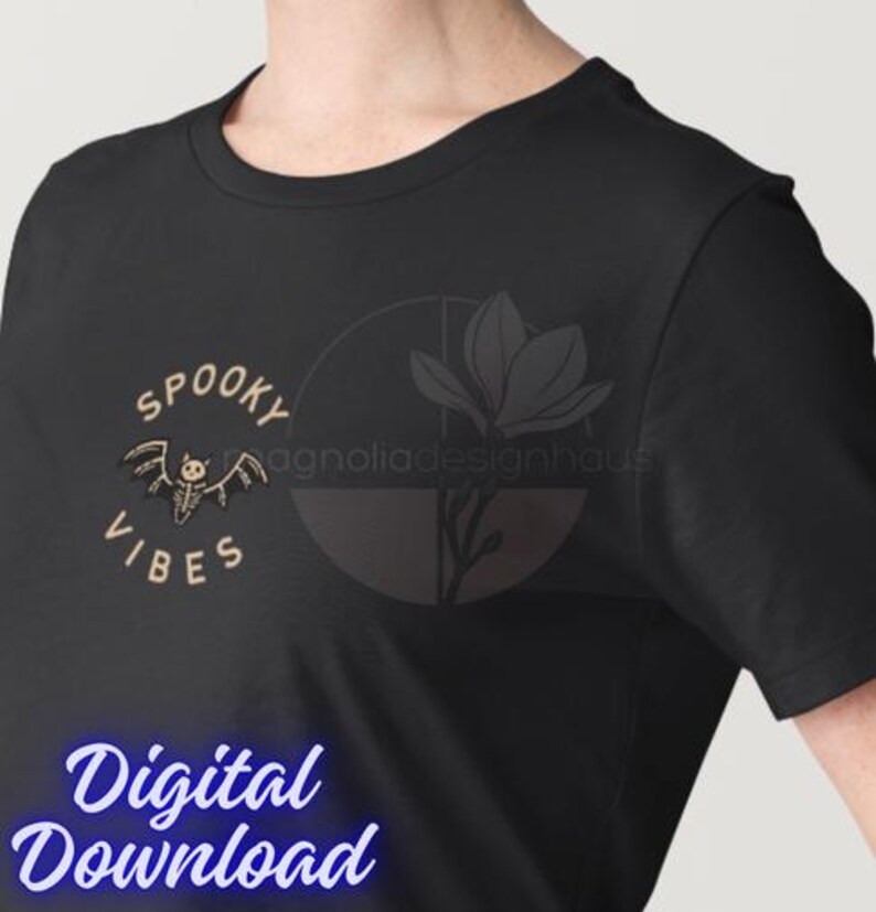 Pu&ograve; includere: T-shirt nero con un design "Spooky Vibes" con una grafica di pipistrello scheletro. Il testo "Digital Download" &egrave; visualizzato in un carattere blu corsivo. Un logo floreale &egrave; visibile sul lato destro della maglietta.