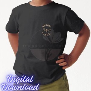 Pu&ograve; includere: T-shirt nera con grafica oro e bianca di un pipistrello, un fiore e le parole "Spooky Vibes". La maglietta presenta anche il testo "magnoliadesignhau" e "Digital Download" in carattere azzurro.
