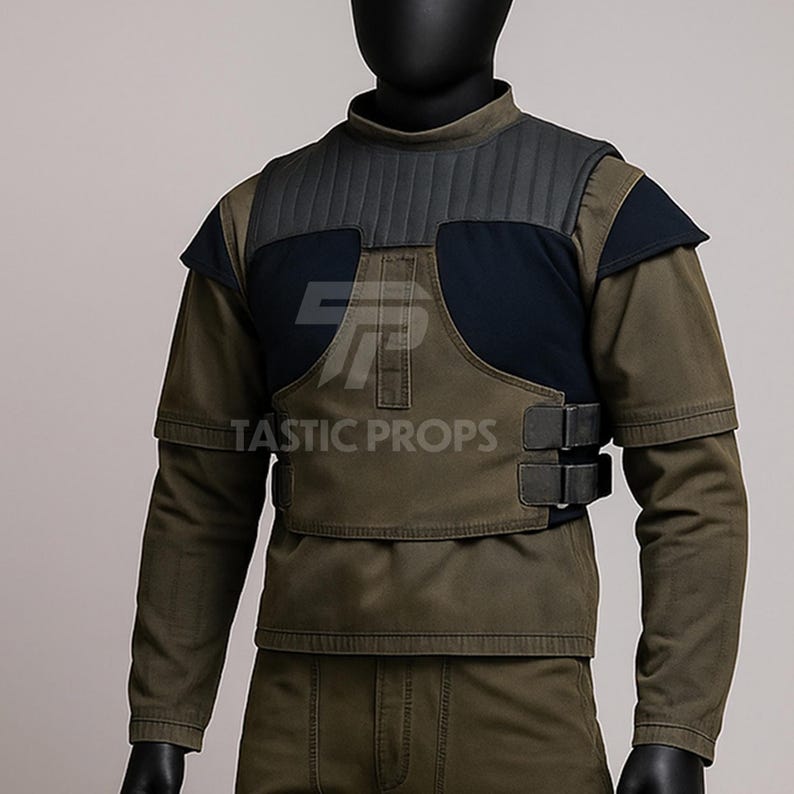 May include: Olive green and navy blue tactical vest with the text "TASTIC PROPS". The vest has a padded collar and shoulder accents, with two black buckles on the front. The long-sleeved shirt underneath is olive green.