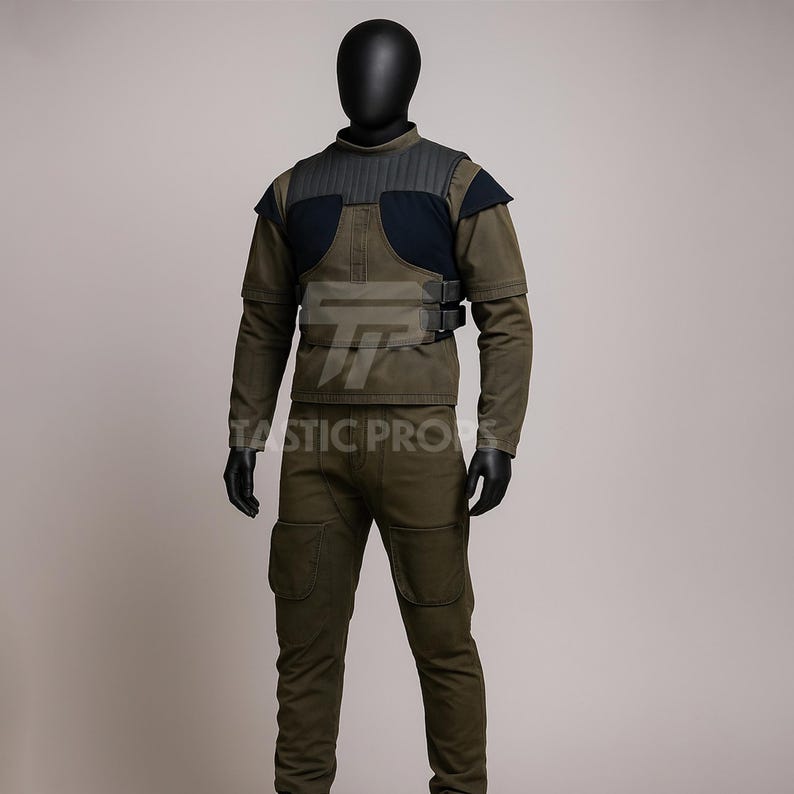 May include: Olive green military-style uniform, including a jacket with a black padded shoulder detail and a matching pair of pants. The jacket has a black panel on the chest and is secured with two black buckles. The text "TASTIC PROPS" is visible on the front.
