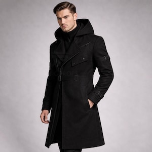 May include: A black hooded coat with a double-breasted design. The coat features a belt at the waist, pockets, and straps on the sleeves. The coat is made of a thick, textured material.