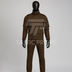 Pu&ograve; includere: Un completo tattico marrone esposto su un manichino. Il completo comprende una maglia a collo alto, un gilet e pantaloni. Il testo "TATIC PROPS" &egrave; visibile nella parte inferiore dell'immagine.
