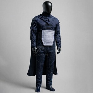 May include: A dark blue costume displayed on a mannequin. The outfit includes a long-sleeved top with a high collar, a cape, and matching pants. A light gray panel is on the chest. The costume is from Tastic Props.