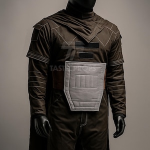 May include: A brown costume with a hood and cape, featuring a gray chest plate and black accents. The costume has long sleeves and is displayed on a mannequin. The stitching is visible, and the overall design suggests a futuristic or sci-fi theme.