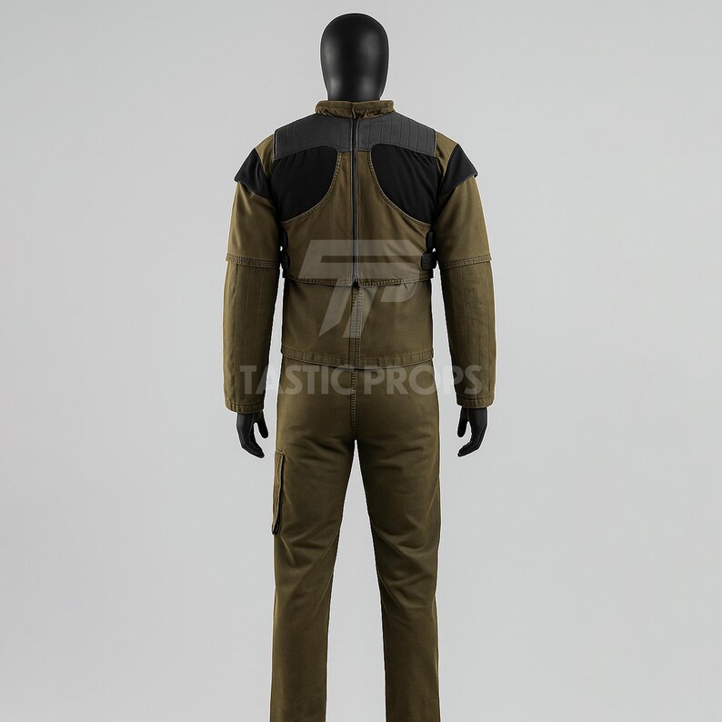 May include: A two-piece olive green jumpsuit with black and gray accents on the shoulders and upper back. The jumpsuit has a high collar and multiple pockets. The text "TASTIC PROPS" is visible on the lower portion of the image.