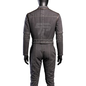 May include: A gray jumpsuit with a matching jacket. The jacket has brown trim on the shoulders and a geometric pattern on the sleeves. The jumpsuit has visible stitching and a belt at the waist.