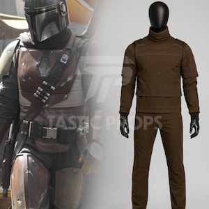 Pu&ograve; includere: Un costume marrone con collo alto, maniche lunghe e pantaloni abbinati, esposto su un manichino nero. Il costume ricorda un personaggio di fantascienza. L'immagine mostra anche un costume Mandaloriano.