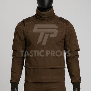 Pu&ograve; includere: Un top marrone a collo alto con pannelli sulle spalle e sul petto. Il top ha maniche lunghe con polsini neri e il testo "TASTIC PROPS" &egrave; visibile. Il top &egrave; esposto su un manichino.