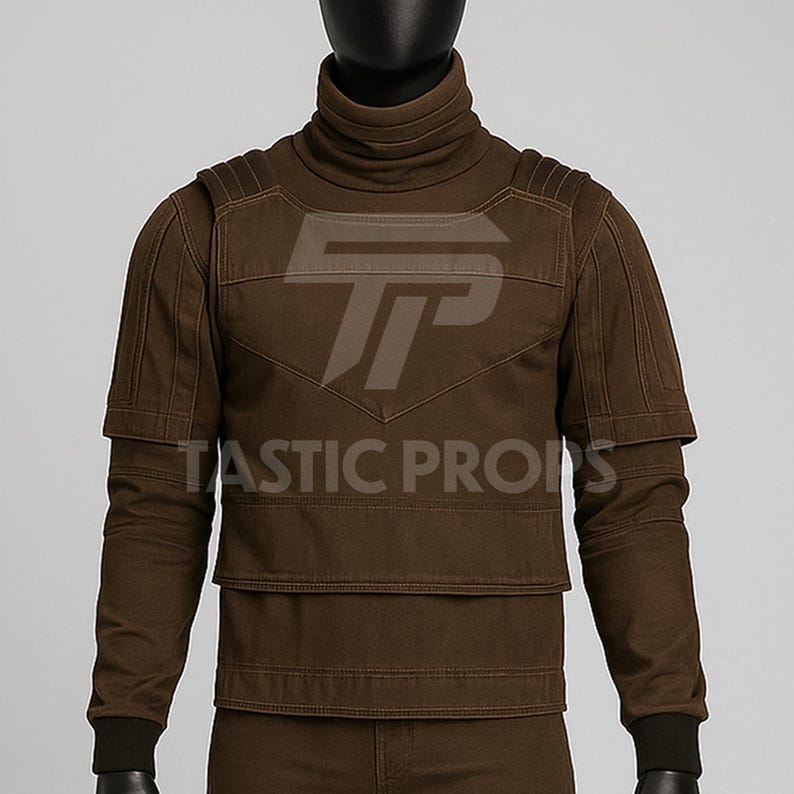 Pu&ograve; includere: Un top marrone a collo alto con pannelli sulle spalle e sul petto. Il top ha maniche lunghe con polsini neri e il testo "TASTIC PROPS" &egrave; visibile. Il top &egrave; esposto su un manichino.
