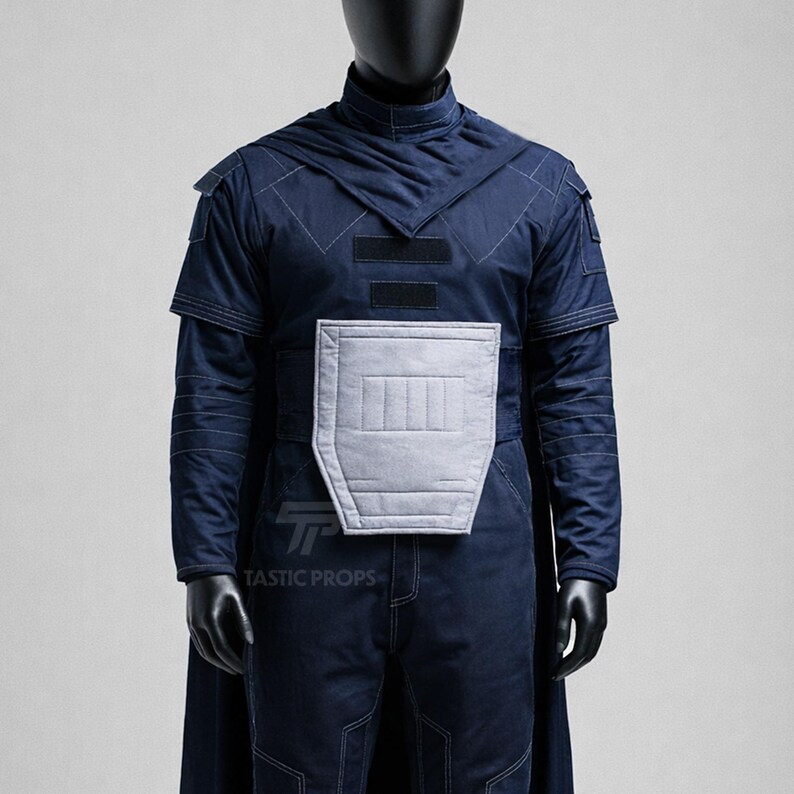 May include: A navy blue costume with a high collar, shoulder pads, and a cape. The costume features a light gray chest plate and is displayed on a black mannequin. The text "TASTIC PROPS" is visible on the costume.