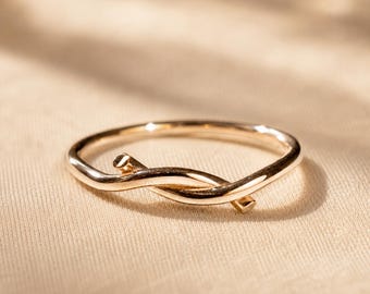May include: A polished gold-tone ring featuring a slender band that curves and overlaps itself at the front, creating a continuous, fluid knot-like design with rounded, smooth ends that taper slightly where they meet the main circular band.