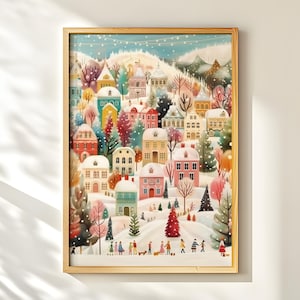 Peut inclure: Une impression encadrée représentant un village d'hiver coloré. L'œuvre présente des maisons enneigées de différentes couleurs, dont le rose, le bleu et le jaune, avec des personnages marchant dans la neige. L'impression est encadrée dans un cadre en bois brun clair.