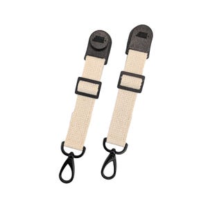 May include: Two cream-colored canvas straps with black plastic hardware. Each strap has a black plastic buckle, a black plastic swivel hook, and a black plastic top piece. The straps are designed for use with a bag or other item.