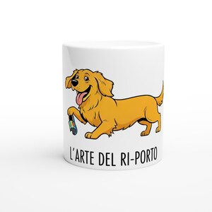 May include: White ceramic mug featuring a cartoon golden retriever dog holding a colorful toy. The dog is smiling with its tongue out. The text "L'ARTE DEL RI-PORTO" is printed in black below the dog.