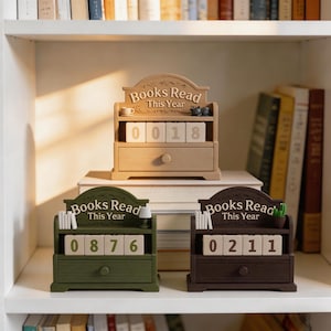 Puede incluir: Piezas decorativas de madera con tem&aacute;tica de libros con el texto "Books Read This Year" y bloques de n&uacute;meros. Las piezas son en tonos marr&oacute;n, verde y marr&oacute;n oscuro. Los n&uacute;meros en los bloques son 0018, 0876 y 0211.