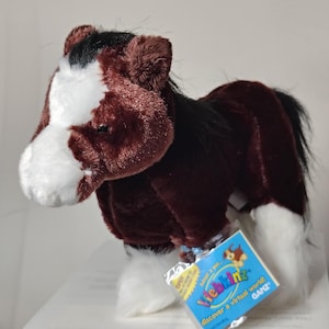 May include: A soft toy horse, predominantly brown with white markings on its face and legs, and a black mane and tail. It has a tag that reads "Webkinz" and "Discover a Virtual World!"