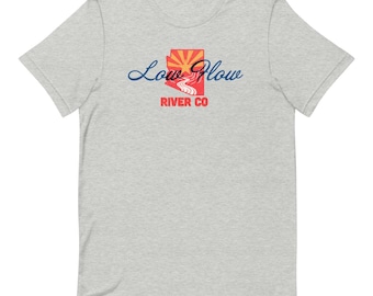 May include: A light gray t-shirt featuring the text "Low Flow" in a cursive font, with a graphic of a sunset and river. The text "River CO" is below the graphic. The shirt is made of a soft material.