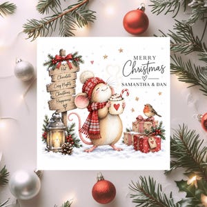 May include: A square Christmas card illustration featuring a mouse wearing a red knit hat and scarf, holding a mug with a candy cane. Beside the mouse is a wooden sign reading Hot Chocolate, Cosy Nights, Christmas Happiness, a lantern, and gifts.
