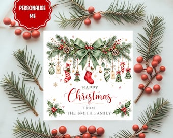May include: A square Christmas card featuring a green bow, pine branches, red berries, and hanging ornaments including stockings and trees. The text reads Happy Christmas from The Smith Family. A red badge in the corner says Personalise Me.