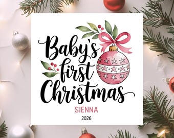May include: A square white sign featuring the black script text Baby's first Christmas, a pink watercolor Christmas ornament with a pink bow, green leaves, red berries, and the name SIENNA in pink capital letters above the year 2026.